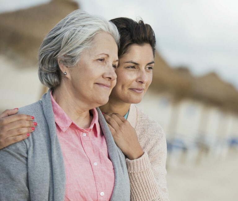 Portrait of mid-adult woman embracing senior mother on beach