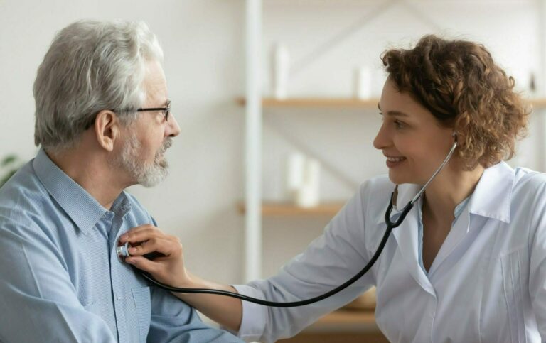 Female doctor listening senior male patient heart using stethoscope