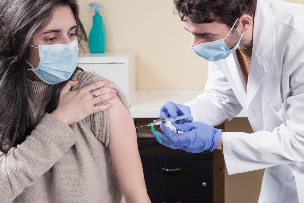 White woman with long hair wearing protective mask while being vaccinated by a doctor using gloves.  Vaccine for the pandemics concept.